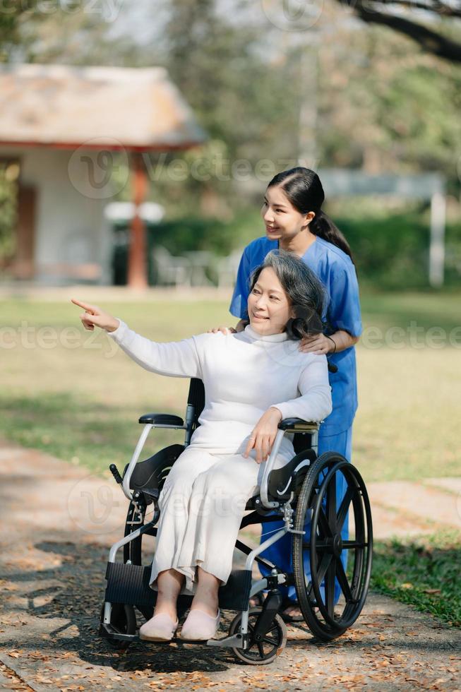 idosos ásia Senior mulher em cadeira de rodas com ásia Cuidado cuidador e encorajar paciente, caminhando dentro jardim. com Cuidado a partir de uma cuidador e Senior saúde seguro. foto