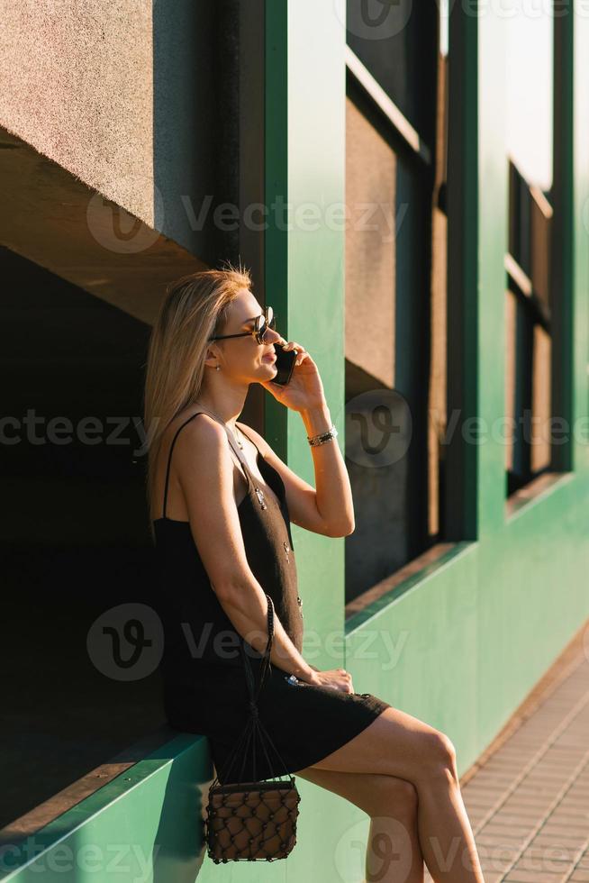 bonita alegre mulher é falando em uma Móvel telefone, caminhando por aí a cidade dentro a verão e relaxante sentado foto