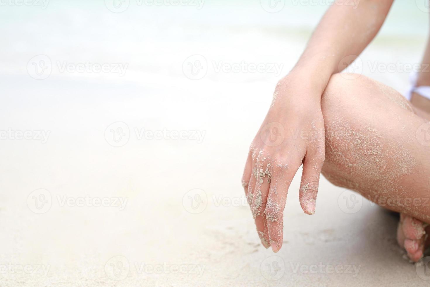 jovem mulher sentado dentro relaxamento ao ar livre em tropical de praia com areia, corpo peças. bronzeada banho de sol menina dentro lótus posição ioga relaxar, e meditação. verão viagem feriado conceito. foto