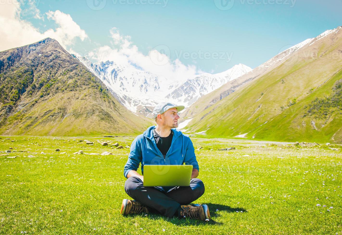 caucasiano bonito cara digital nômade sentar trabalhos tipo em computador portátil com montanhas fundo. digital nômade viajante blogging em viagens. Ideias e trabalhos conectados dentro postar pandemia mundo. foto