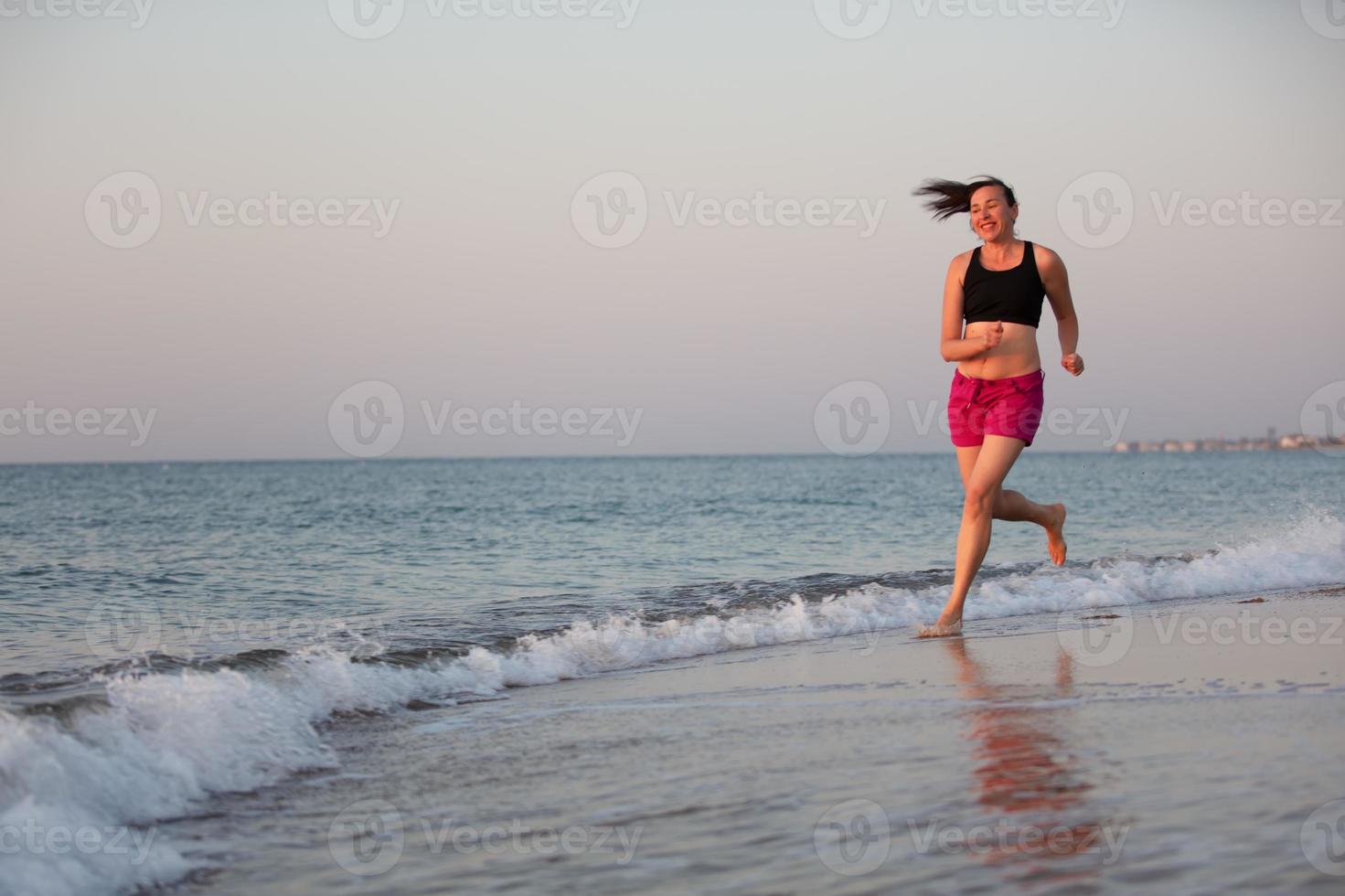 uma meia idade mulher corrida ao longo a costa. Esportes às mar adulto mulher. foto