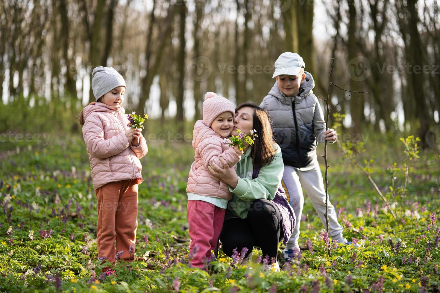 feliz mãe dia. nós amor você, mãe. mãe com uma ramalhete do flores e três crianças dentro Primavera florescendo floresta. foto