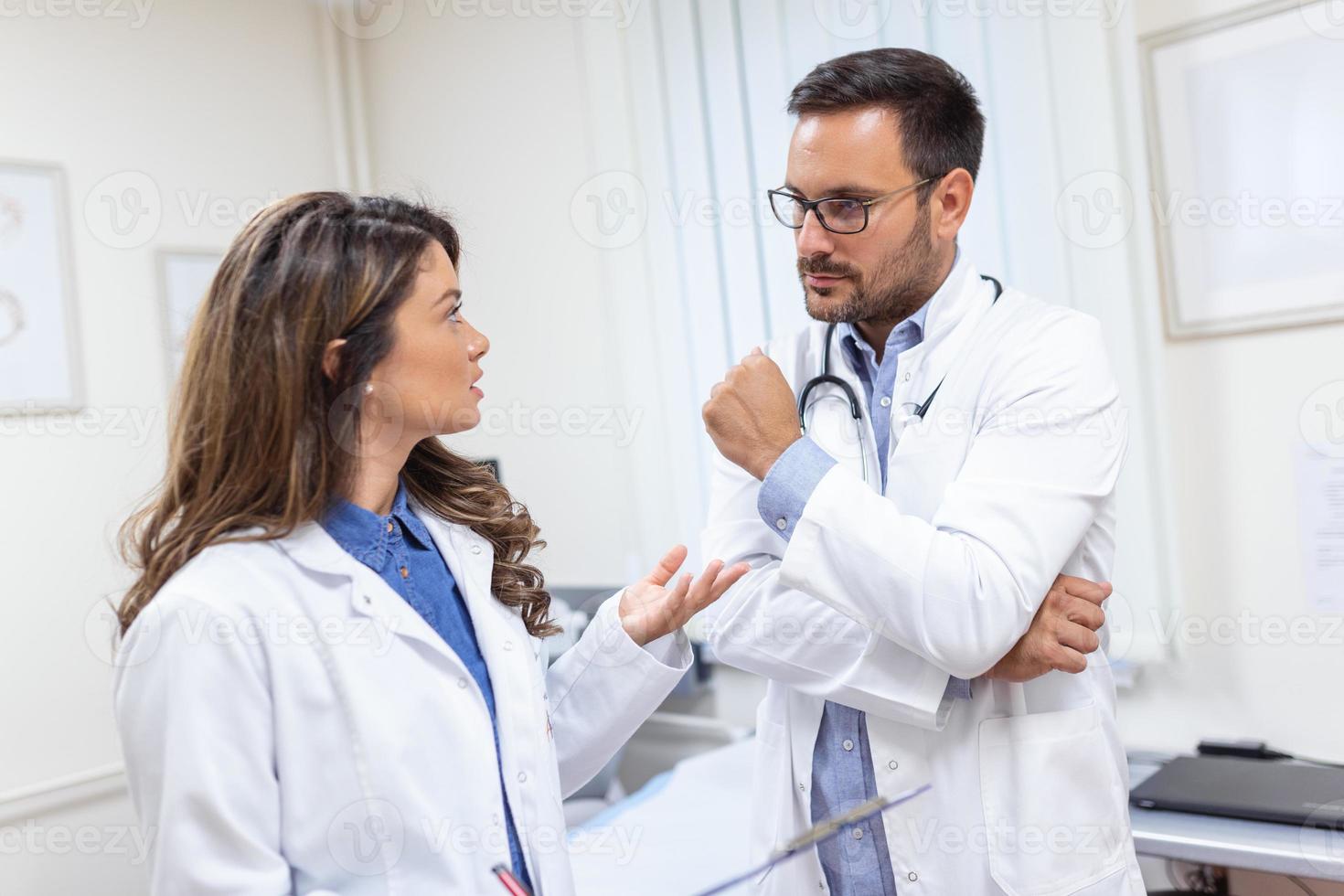 dois médico colegas dentro branco casacos, segurando prancheta. elas estão tão bem-sucedido, sorrir e trabalhos dentro equipe juntos foto