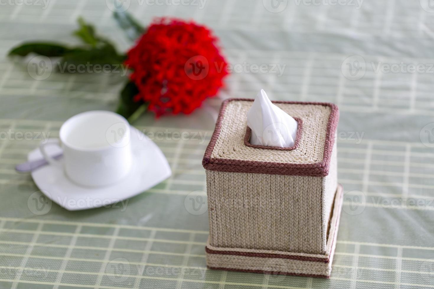 cru fibra cor feito à mão guardanapo caixa em a jantar mesa com uma vermelho flor e uma branco xícara de chá. lenço de papel papel caixa em restaurante. foto