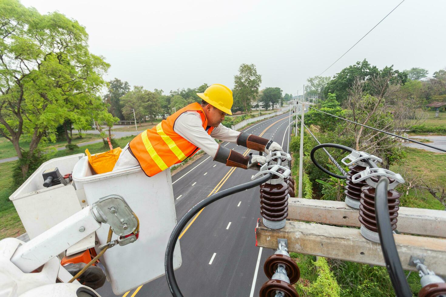 ásia eletricista com guindaste caminhão é instalando cabo linhas e elétrico transmissão em elétrico poder pólo contra azul céu fundo foto