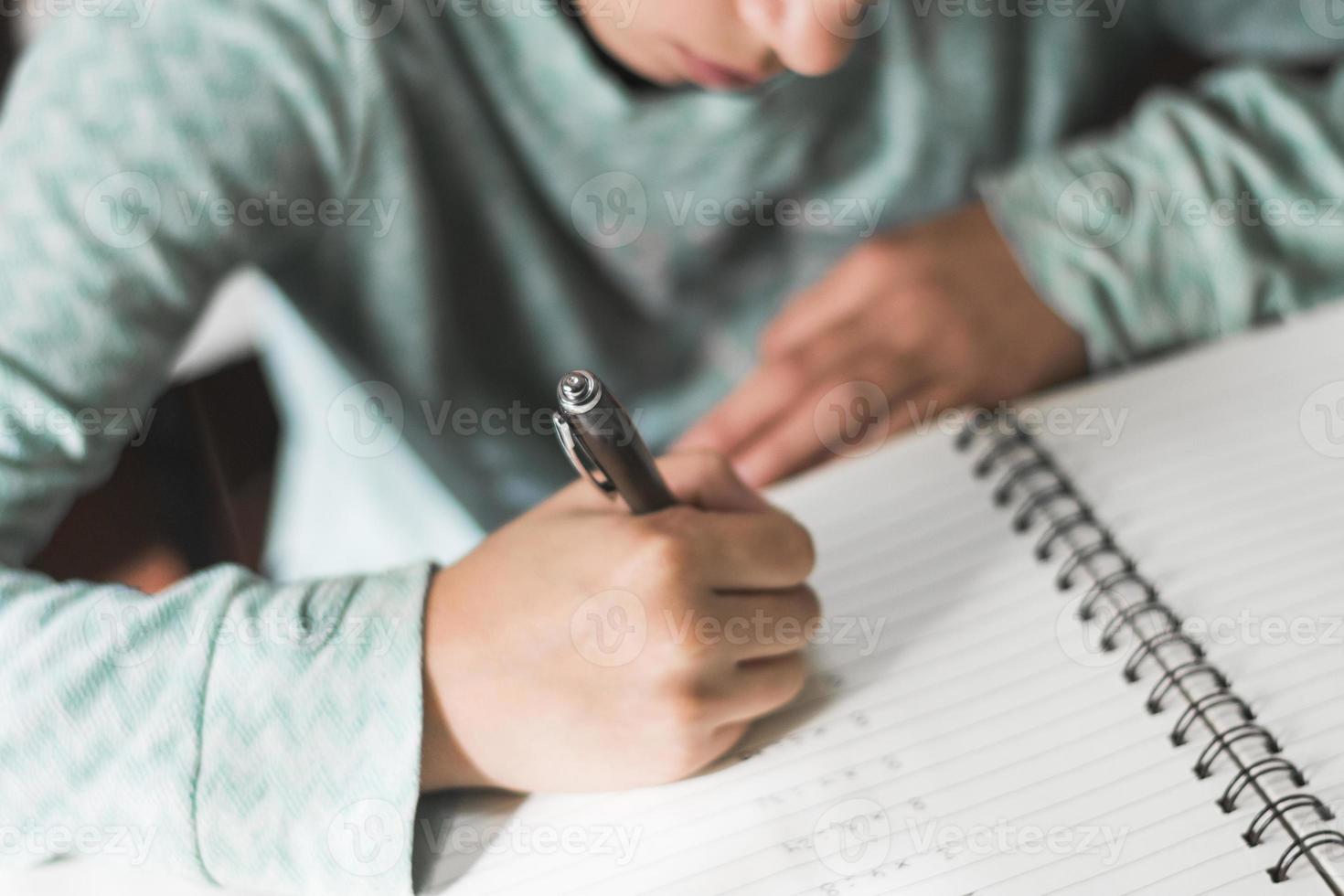 criança cortada escrevendo no caderno foto