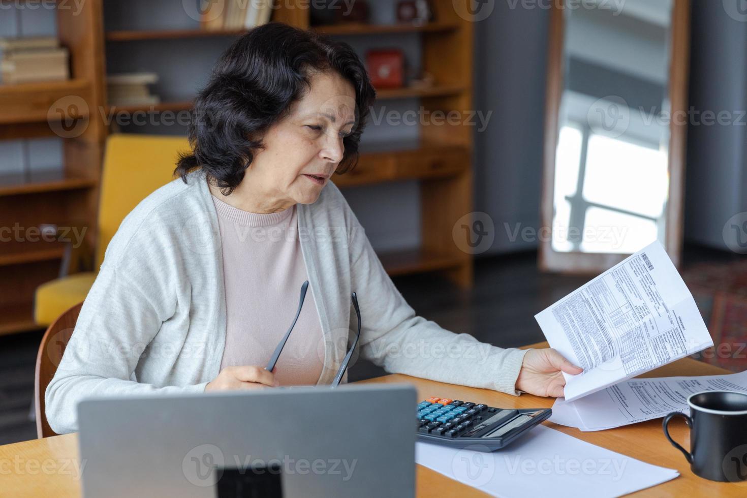 meio envelhecido Senior mulher sentar com computador portátil e papel documento, pensativo Mais velho maduro senhora lendo papel conta pagar conectados às casa gerenciando banco finanças calculando impostos planejamento empréstimo dívida pensão Forma de pagamento foto