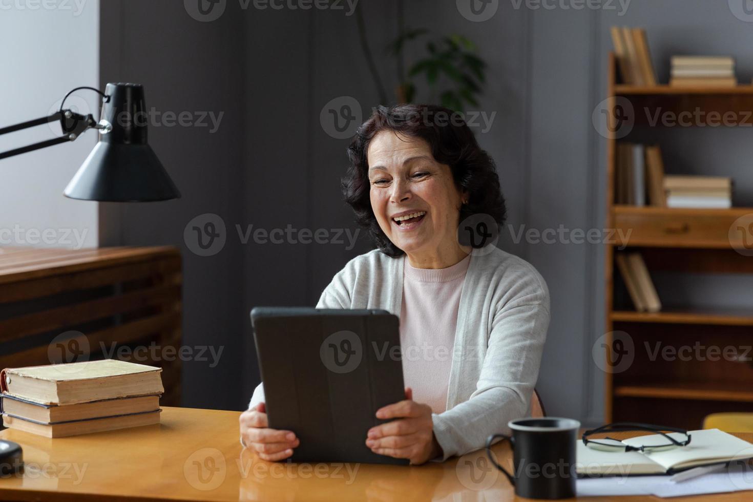 feliz meio envelhecido Senior mulher segurando tábua conversa em vídeo ligar com amigos família. rindo maduro velho Senior avó tendo Diversão falando Falando com crescido acima crianças on-line. foto