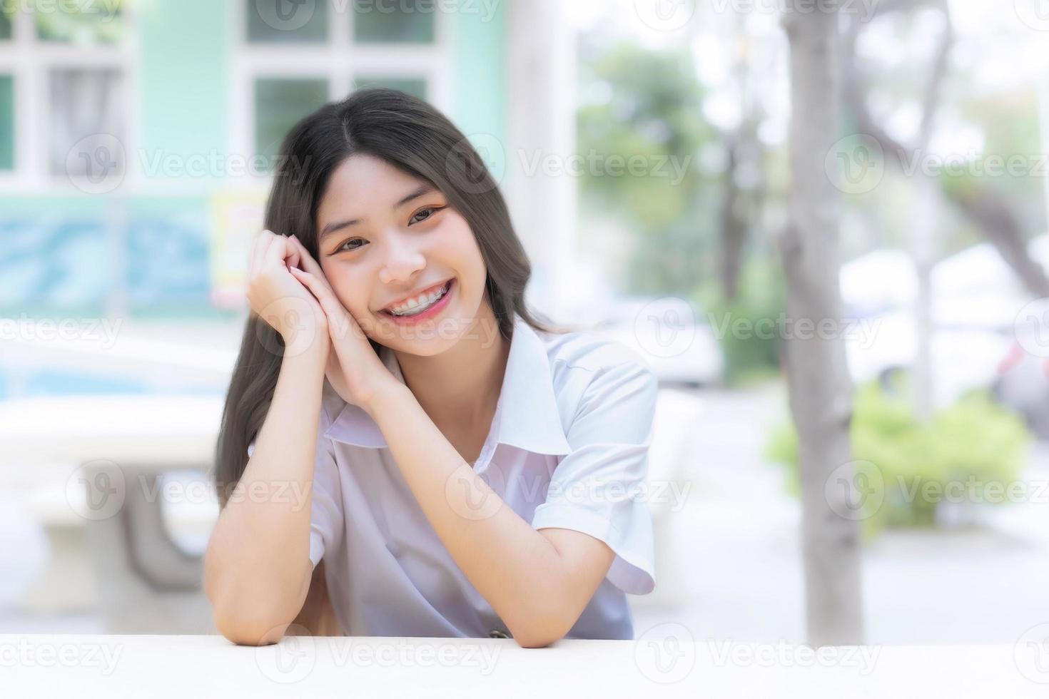 retrato do fofa ásia tailandês menina aluna dentro uma uniforme é sentado sorridente alegremente e com confiança dentro universidade foto