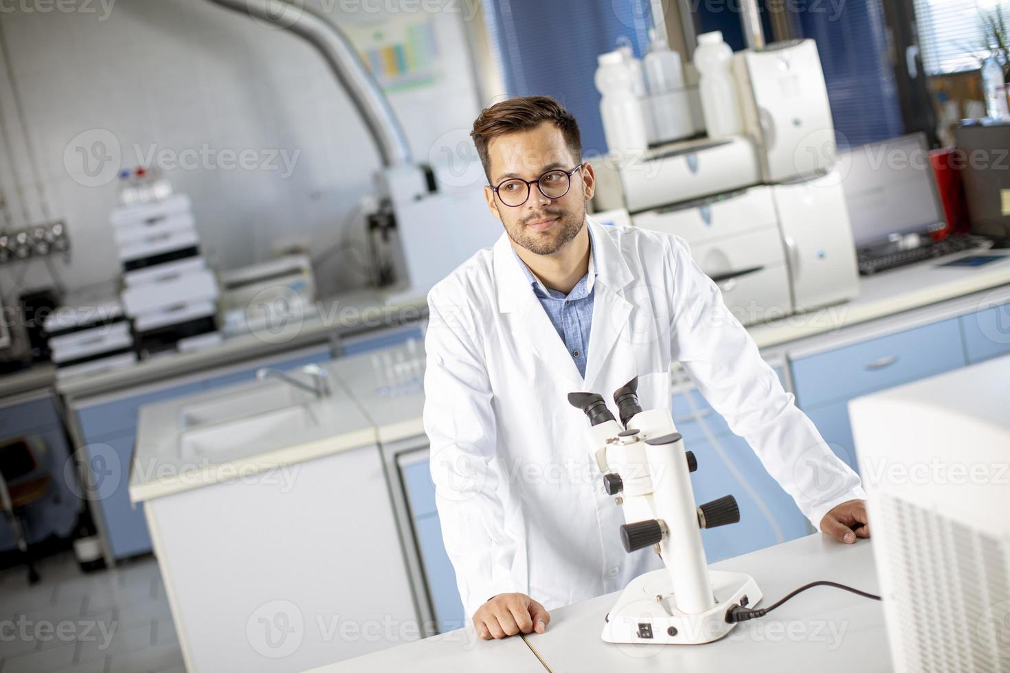 jovem cientista vestindo jaleco branco trabalhando com microscópio binocular no laboratório de ciências materiais foto