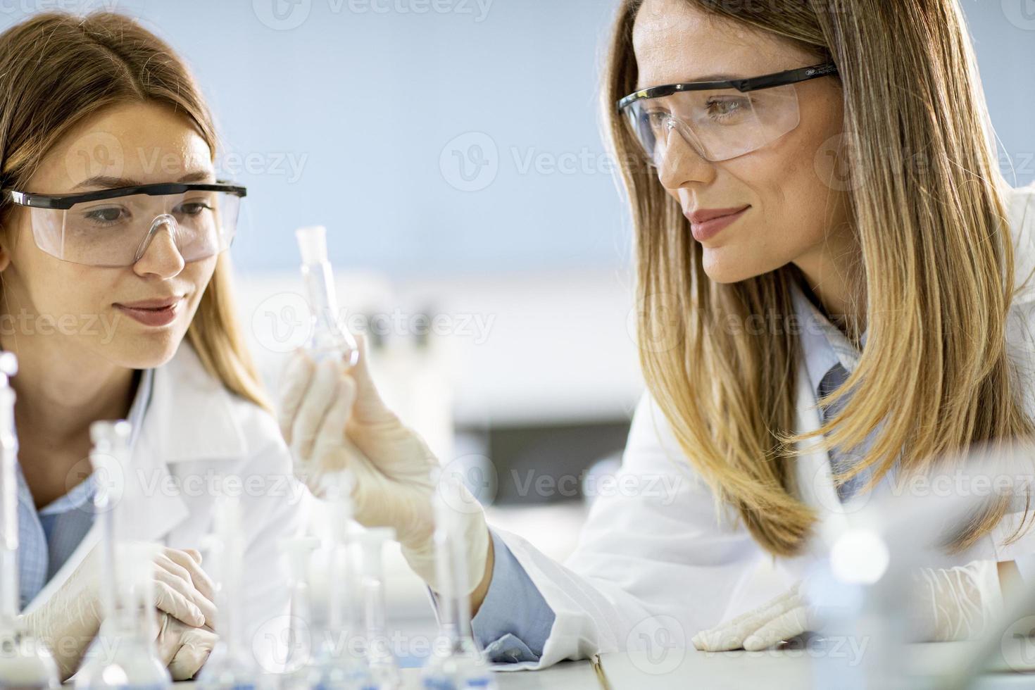 duas mulheres pesquisadoras científicas olhando para frascos com soluções em um laboratório foto