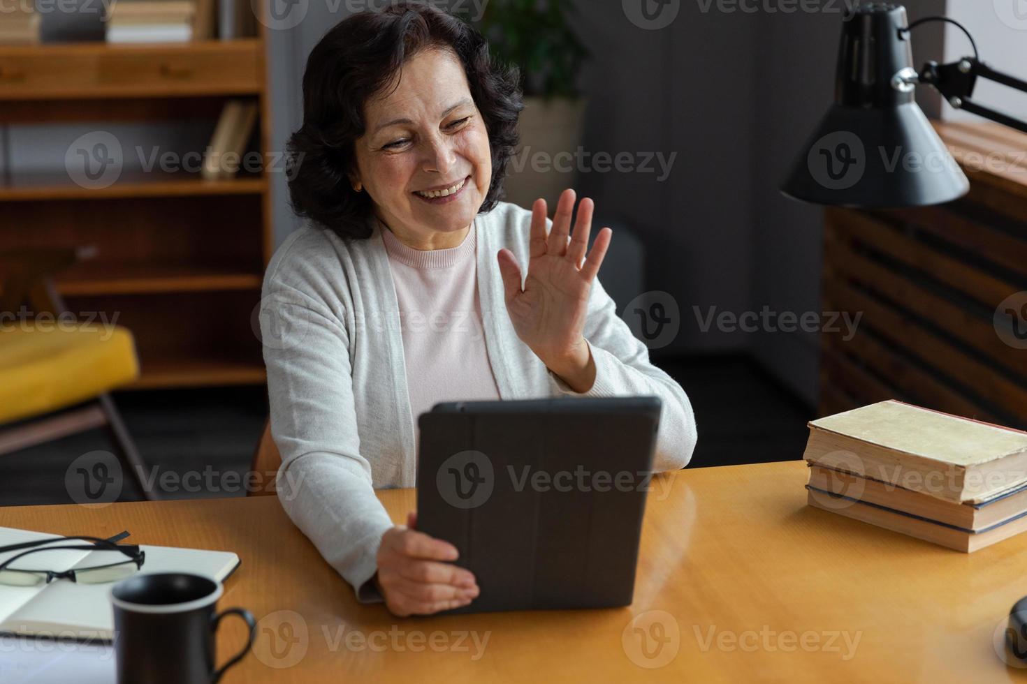 feliz meio envelhecido Senior mulher segurando tábua conversa em vídeo ligar com amigos família. rindo maduro velho Senior avó tendo Diversão falando Falando com crescido acima crianças on-line. foto