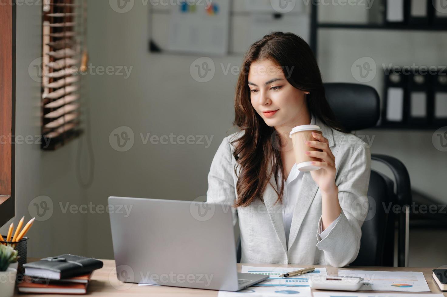 jovem lindo mulher digitando em tábua e computador portátil enquanto sentado às a trabalhando de madeira mesa escritório foto