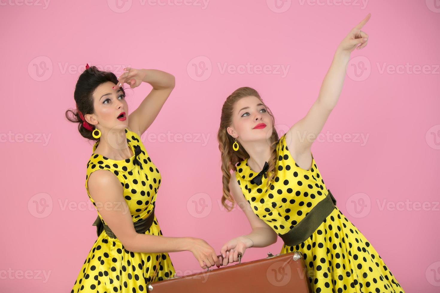 retro viajante meninas com mala. dois mulheres vestido dentro anos cinquenta estilo estão segurando a velho mala. foto