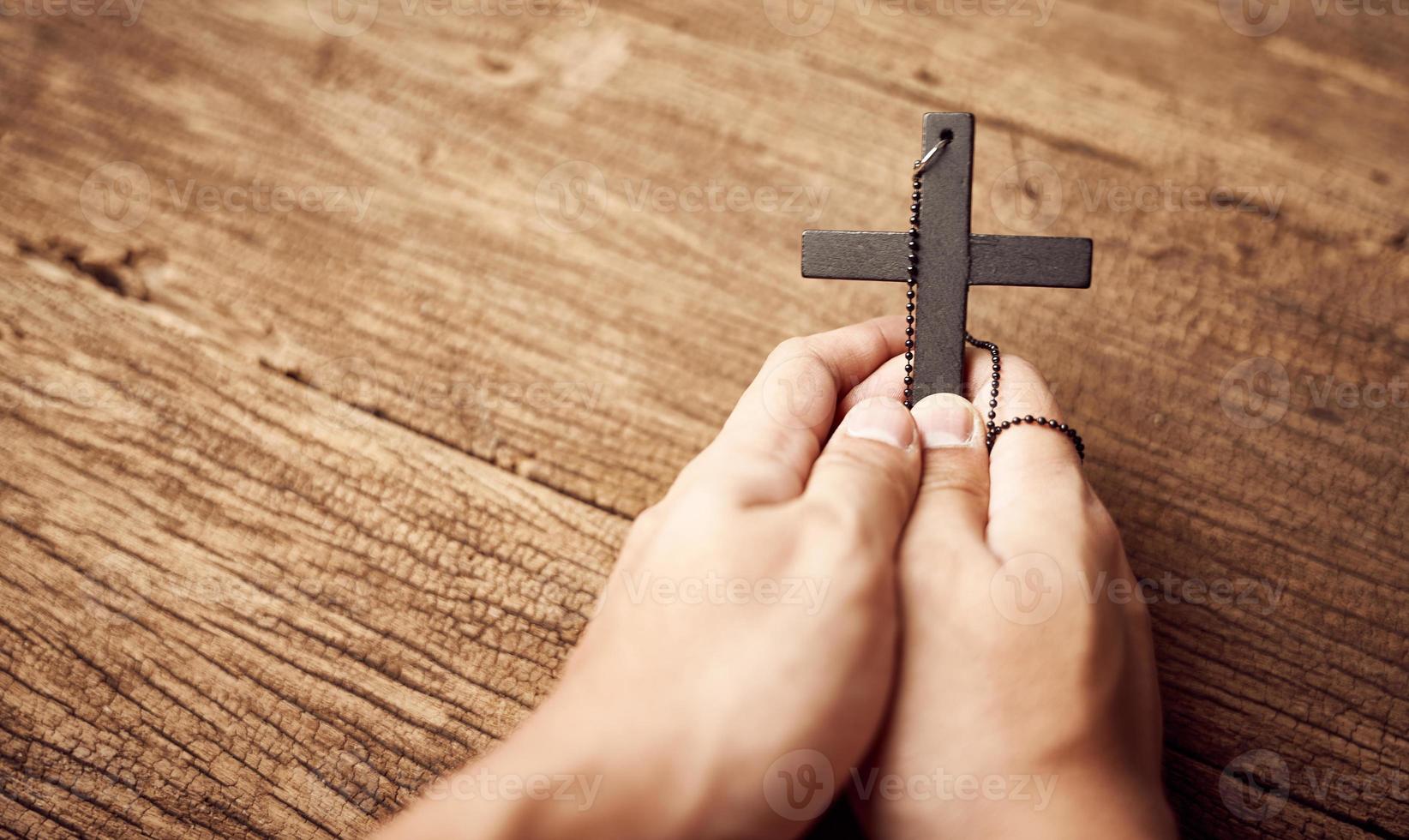 conceito do cristão. fechar acima do mão Rezar segurando uma Jesus Cristo Preto Cruz em a velho de madeira mesa fundo com cópia de espaço foto