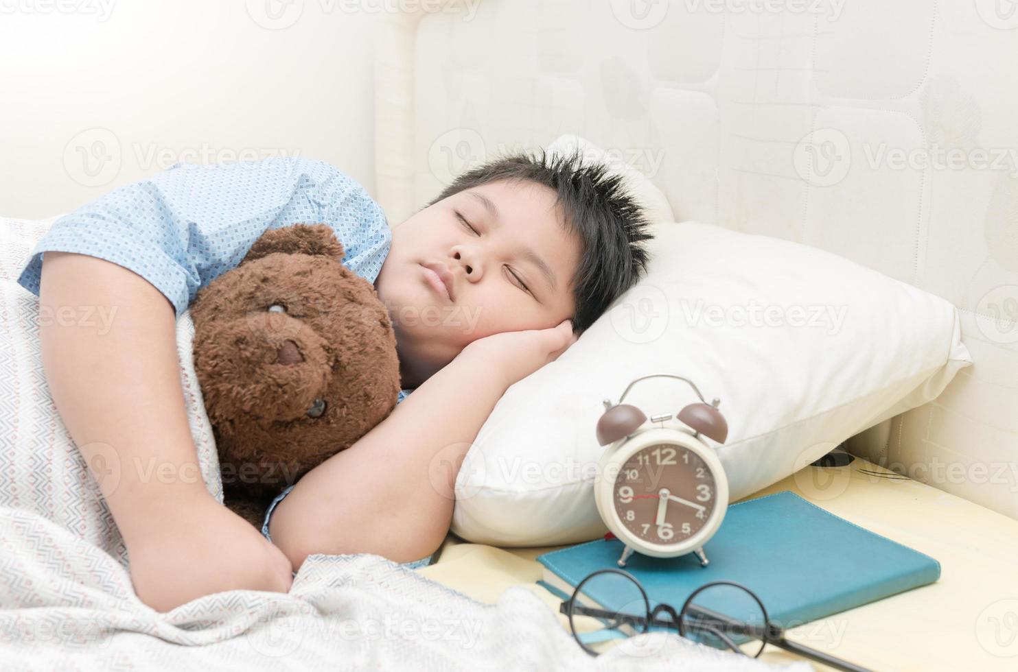 gordo Garoto dormir e abraço Urso de pelúcia Urso em cama foto