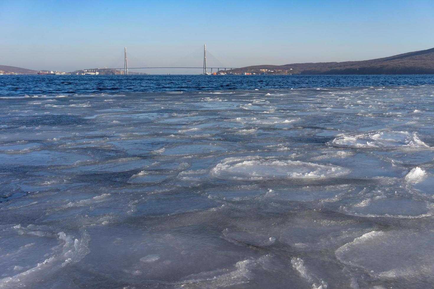 corpo de água coberto de gelo e a ponte russky ao fundo em vladivostok, Rússia foto