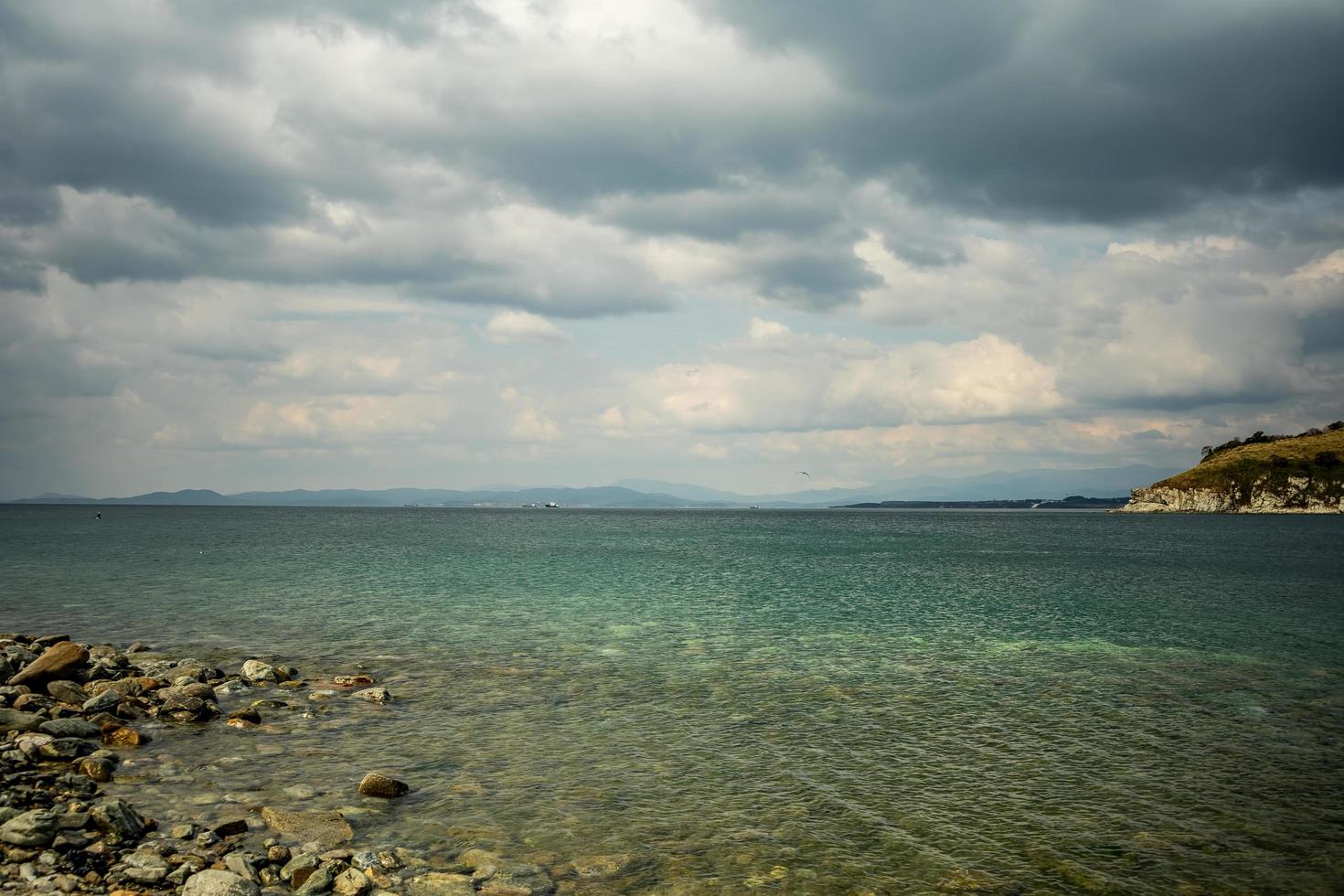 paisagem marinha de uma costa rochosa em um corpo de água com montanhas e céu azul nublado em Nakhodka, Rússia foto