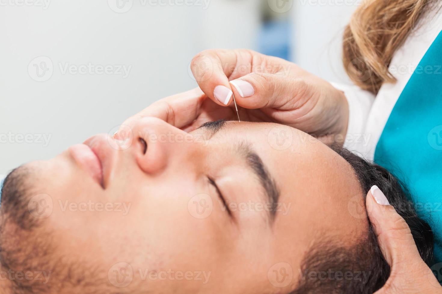 médico realizando facial acupuntura em uma jovem masculino paciente foto