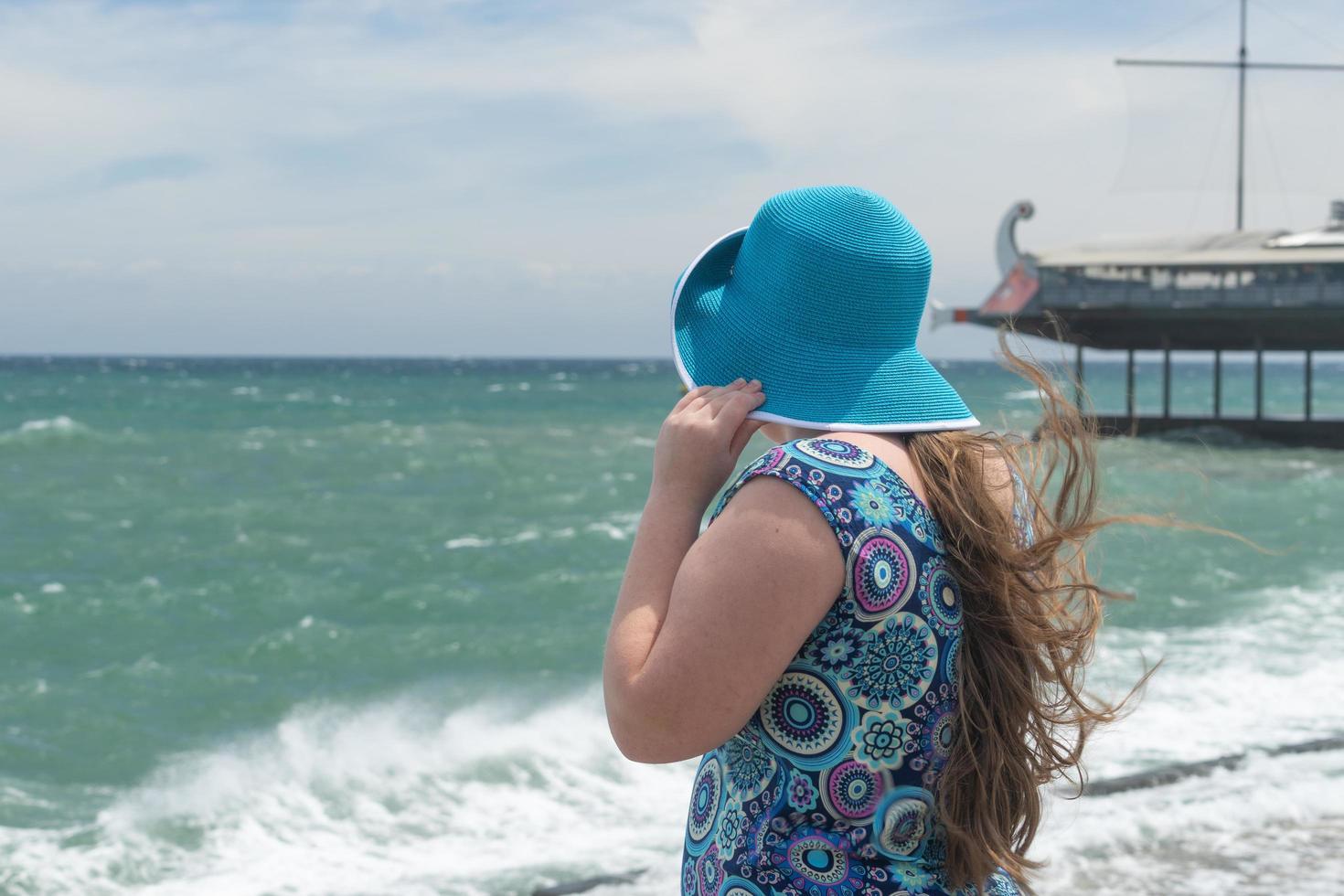 uma garota com um chapéu azul e um vestido colorido em uma praia, olhando para o mar em yalta, na Crimeia foto