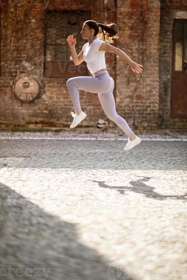 bela jovem pulando alto durante o treinamento no ambiente urbano foto