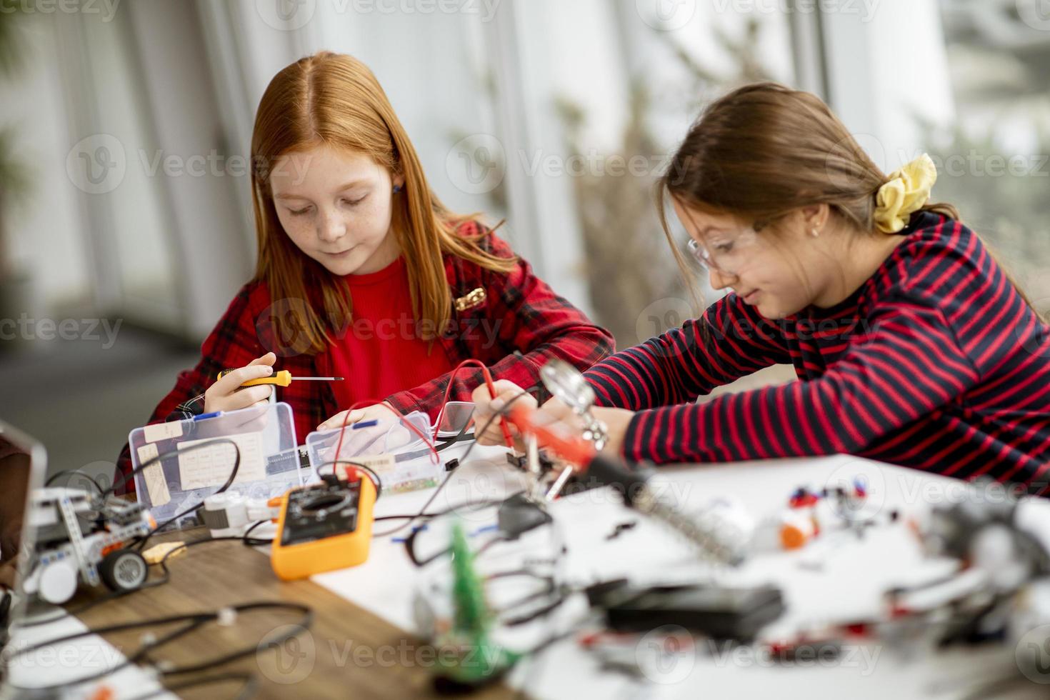 garotinhas fofas programando brinquedos elétricos e robôs na sala de aula de robótica foto