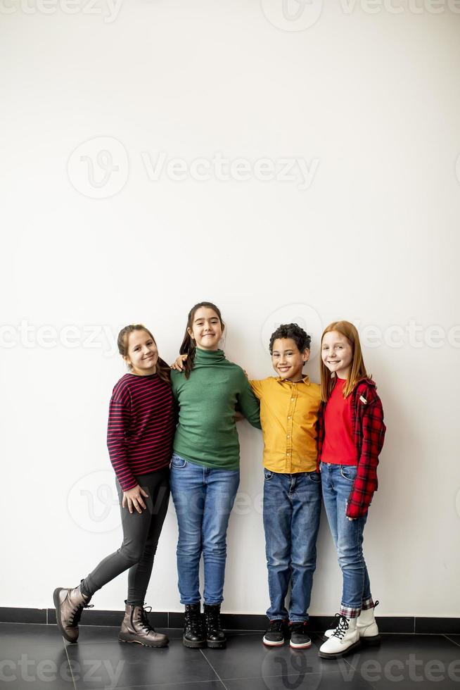 retrato de crianças fofas em jeans, olhando para a câmera e sorrindo, encostado na parede branca foto