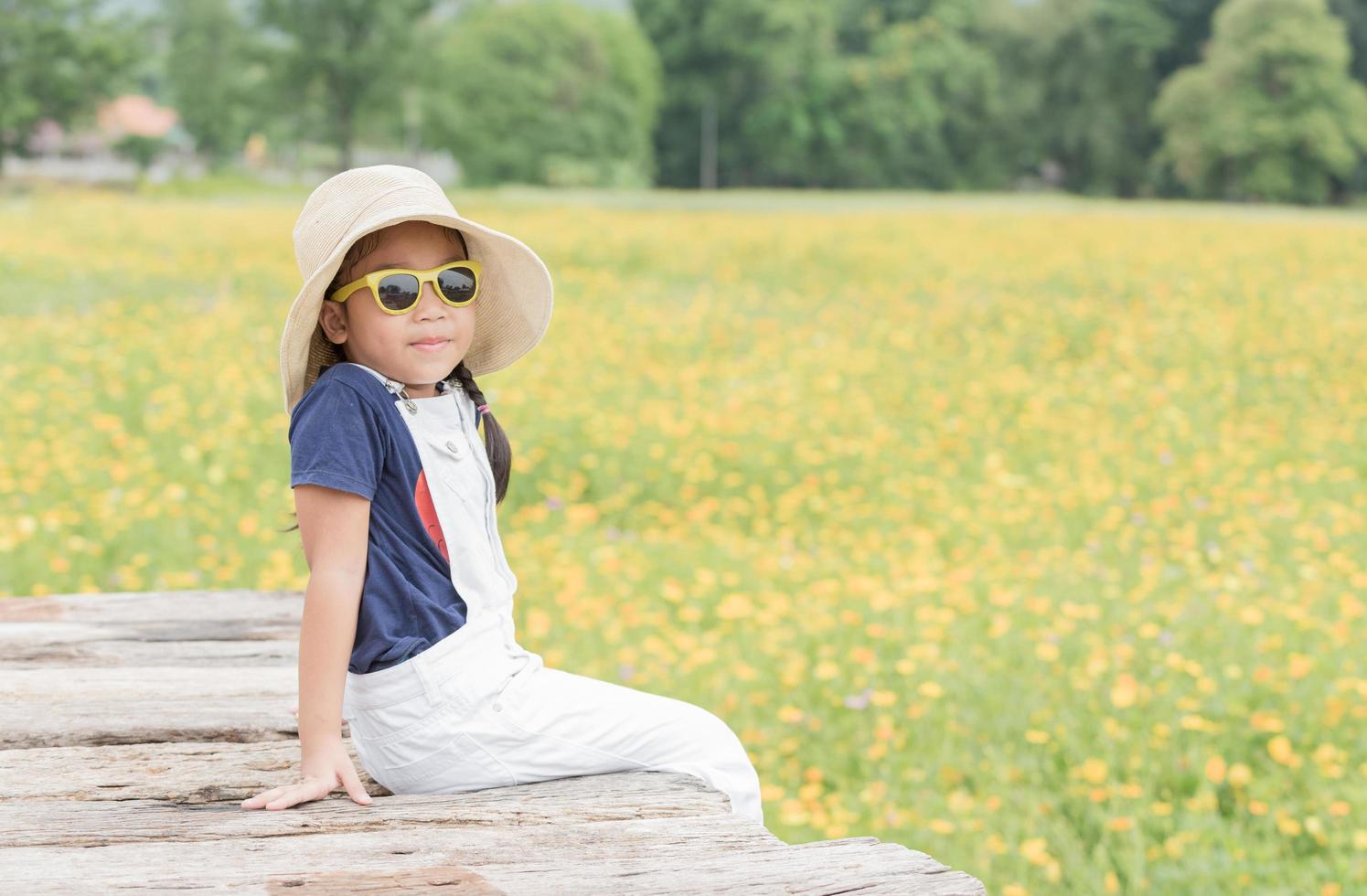 fofa menina sentar em madeira e amarelo flor fundo foto