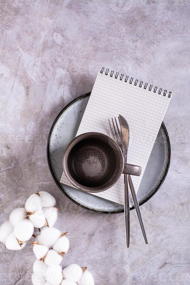 esvaziar cerâmico caneca, talheres e caderno em uma prato em uma cinzento fundo topo e vertical Visão foto