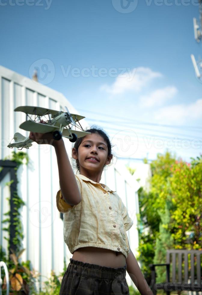 retrato do uma pequeno menina dentro a frente quintal. com modelo aeronave que é a Sonhe do uma criança quem quer para estar uma piloto. foto
