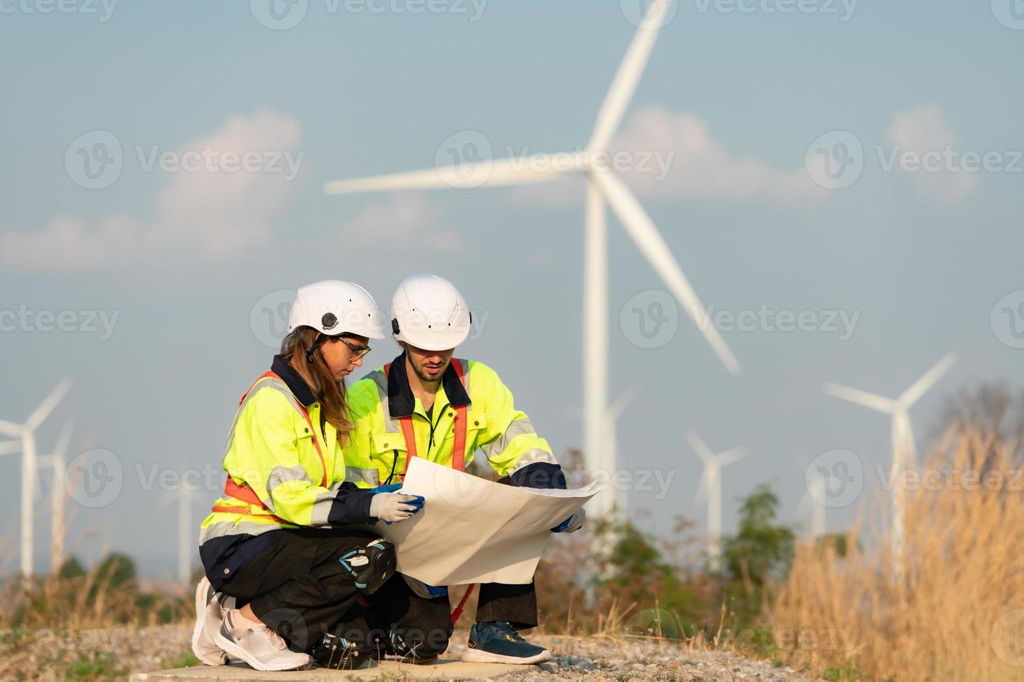 homem e fêmea engenheiro estacionado às a natural energia vento turbina local. com diariamente auditar tarefas do principal vento turbina operações este transformar vento energia para dentro elétrico eletricidade foto