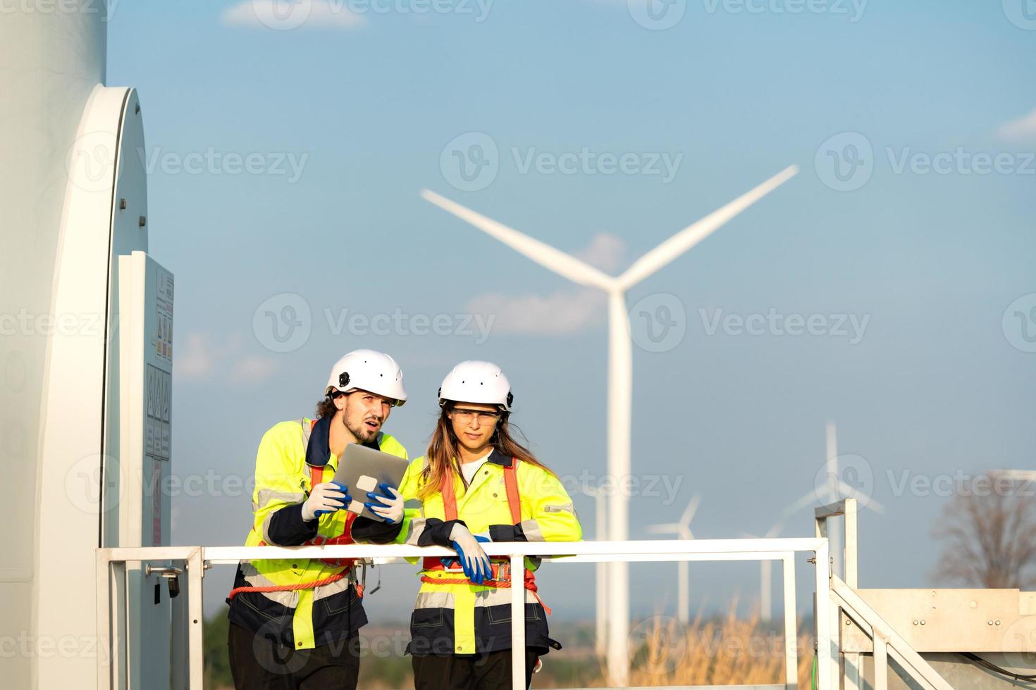 homem e fêmea engenheiro estacionado às a natural energia vento turbina local. com diariamente auditar tarefas do principal vento turbina operações este transformar vento energia para dentro elétrico eletricidade foto