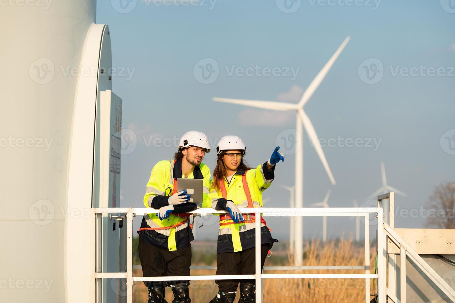 homem e fêmea engenheiro estacionado às a natural energia vento turbina local. com diariamente auditar tarefas do principal vento turbina operações este transformar vento energia para dentro elétrico eletricidade foto