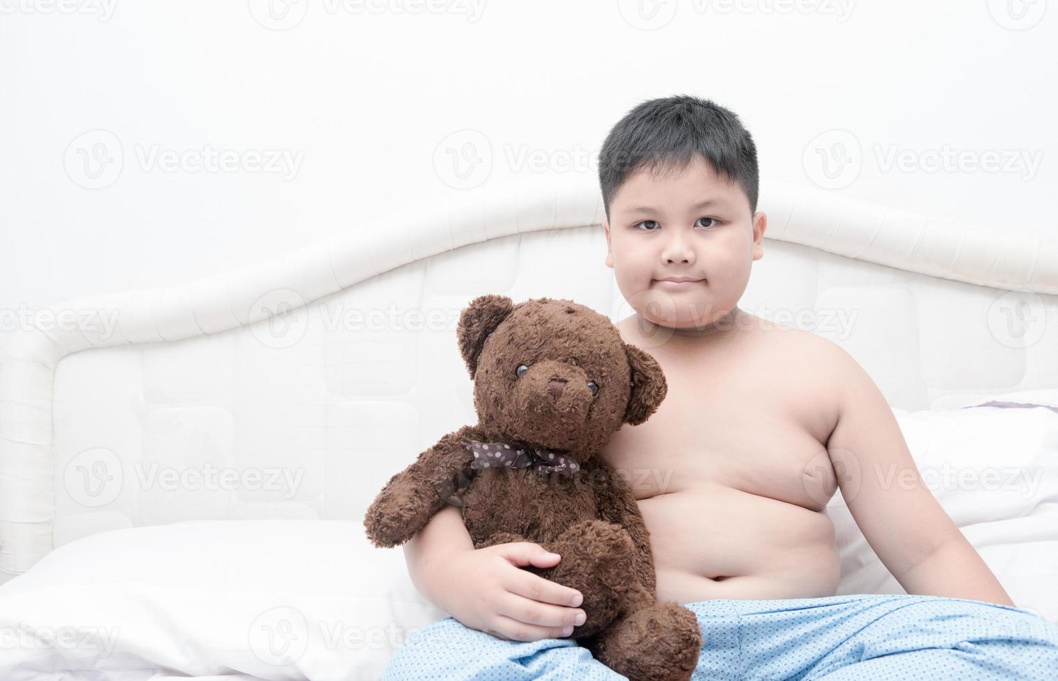 obeso gordo Garoto abraço Urso de pelúcia Urso em cama foto