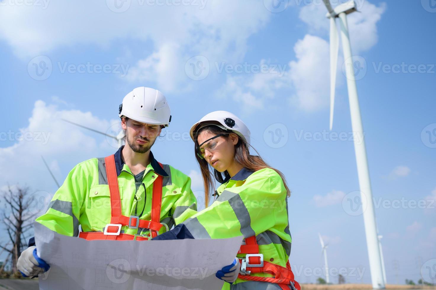 homem e fêmea engenheiro estacionado às a natural energia vento turbina local. com diariamente auditar tarefas do principal vento turbina operações este transformar vento energia para dentro elétrico eletricidade foto