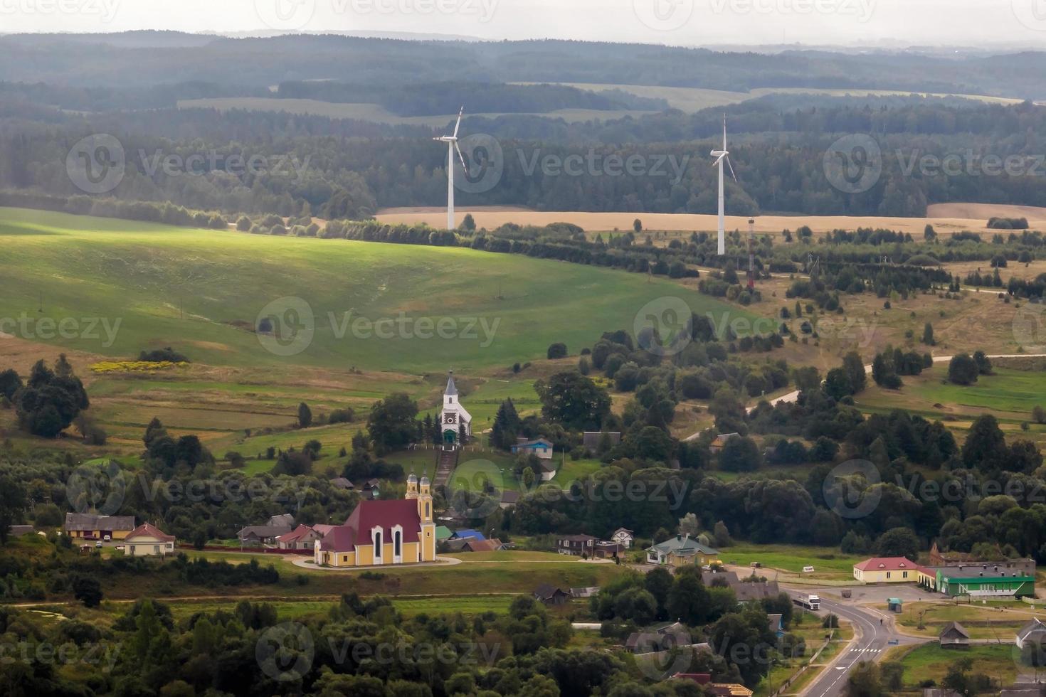 aéreo panorâmico Visão do verde Vila com casas, celeiros e cascalho estrada dentro floresta com moinhos de vento foto