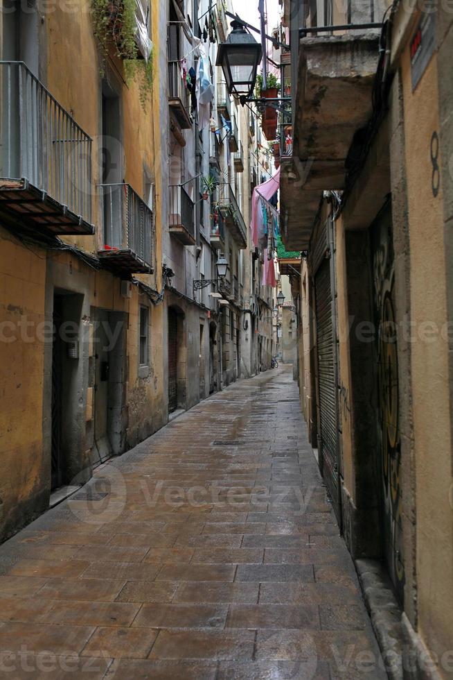 limitar rua, Alto paredes do casas, úmido pedra pavimento, panelas do flores em a varandas e roupas secagem foto