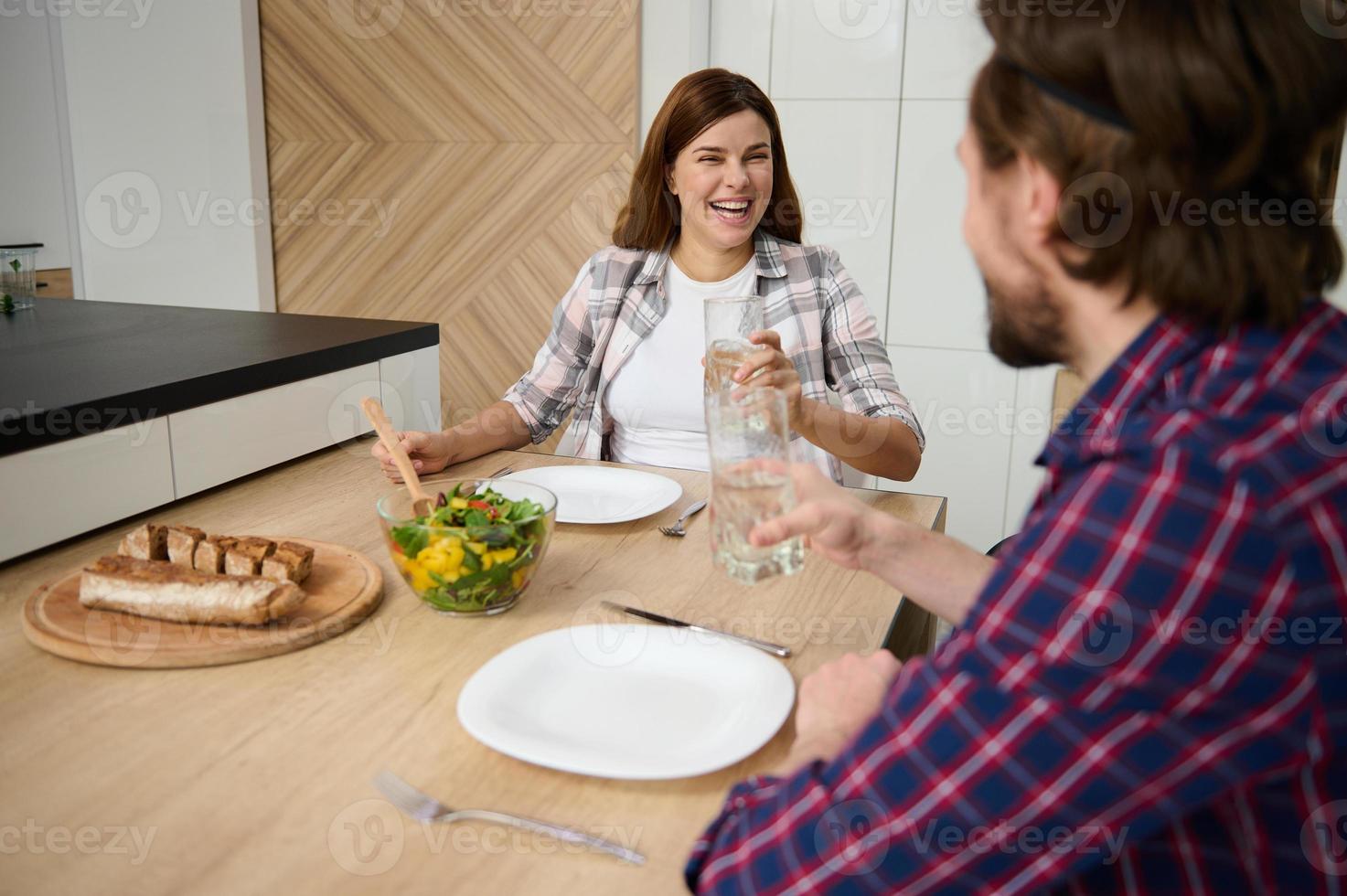 diariamente estilo de vida do uma lindo feliz jovem caucasiano casal desfrutando almoço junto, tendo Diversão discussão e rindo enquanto sentado às mesa dentro a casa foto