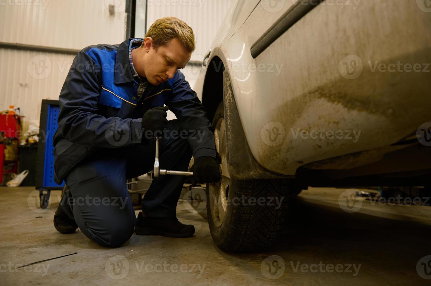 jovem caucasiano auto mecânico verificação carro roda dentro auto serviço garagem. mecânico manutenção engenheiro trabalhando dentro automotivo indústria. automóvel manutenção e reparar conceito foto