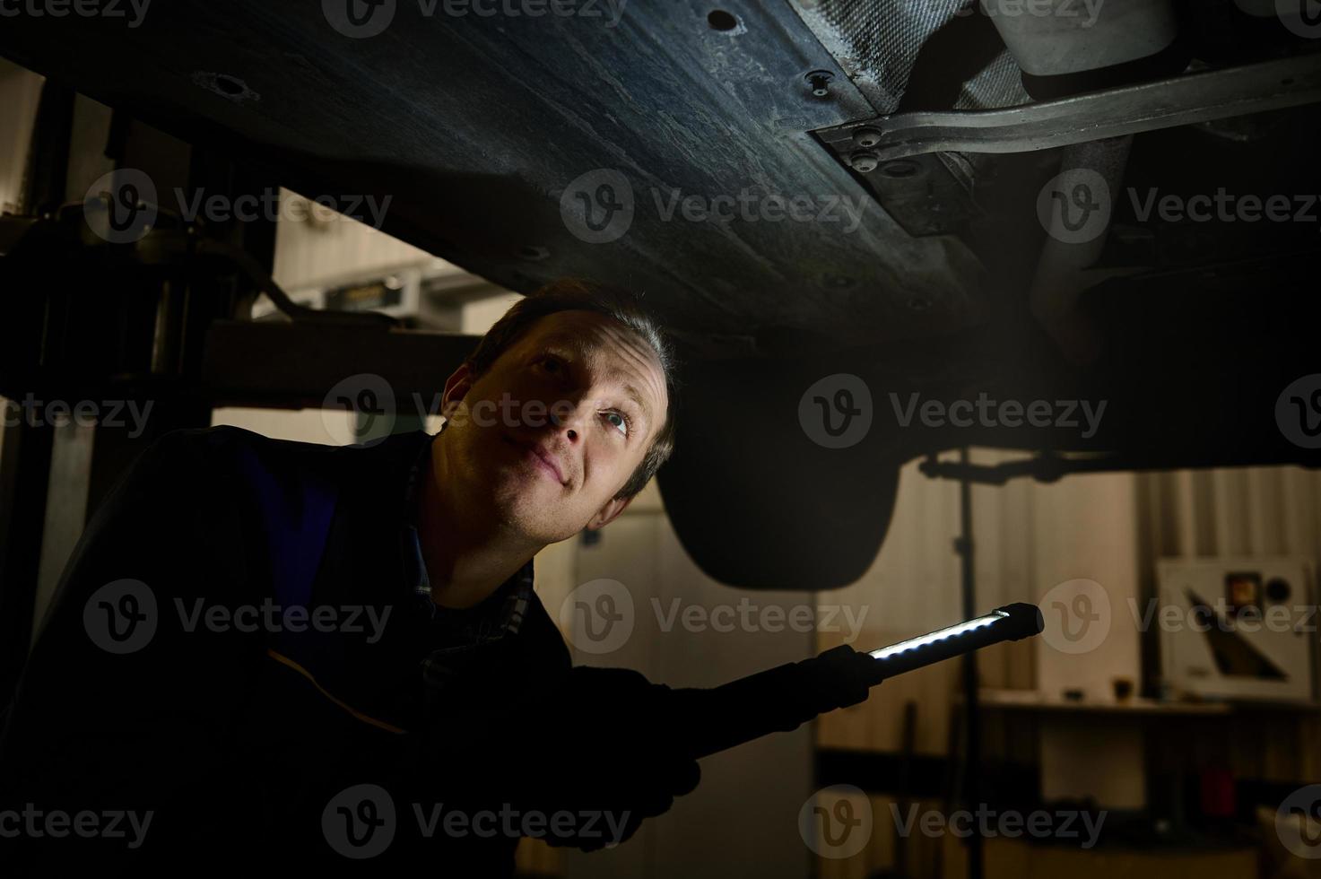 técnico verificação moderno carro às automóvel reparar fazer compras. auto mecânico usando uma lanterna luminária para inspecionando a parte inferior do corpo do a levantado carro dentro uma carro serviço. automóvel manutenção conceito foto