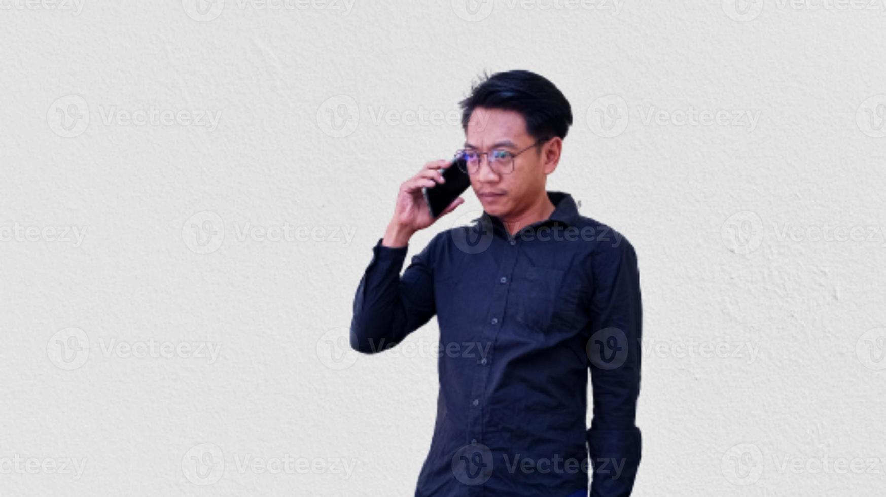 selecionado foco retrato do uma confuso ásia homem vestindo Preto camisa segurando dele Móvel telefone, isolado em branco fundo. foto