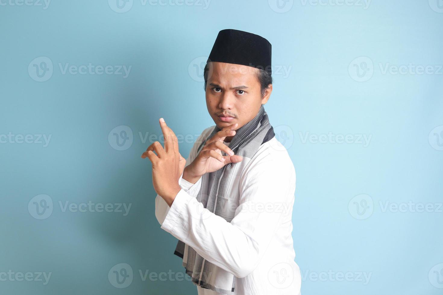 retrato do ásia muçulmano homem dentro branco Koko camisa fazendo marcial artes gesto ou pencak silat. isolado imagem em azul fundo foto