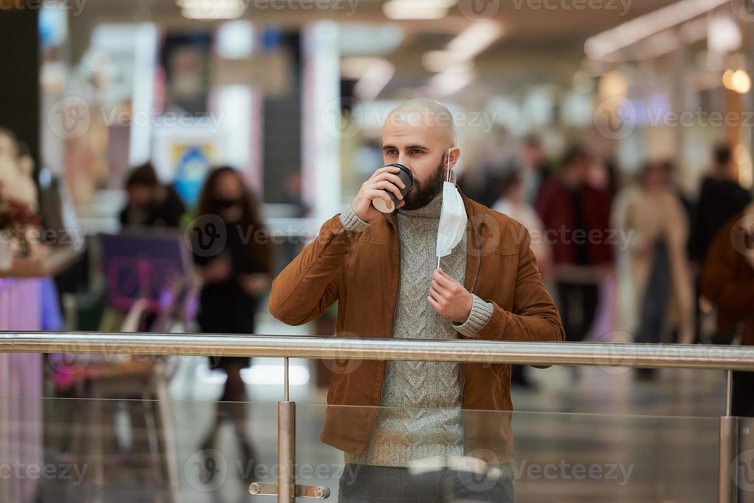 um homem está segurando uma máscara decolada enquanto bebe café no shopping foto