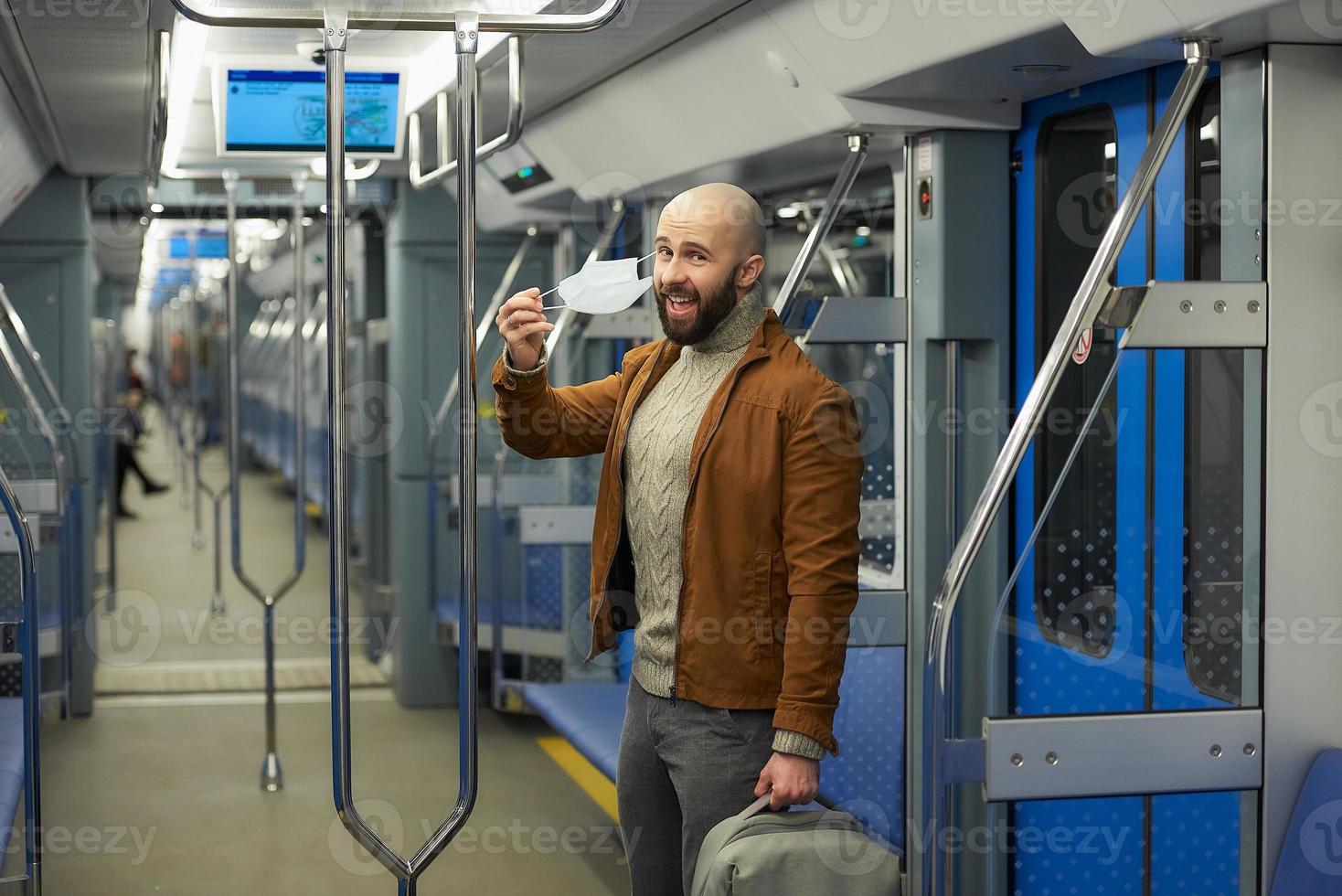 um homem com barba está tirando uma máscara médica e sorrindo em um trem foto