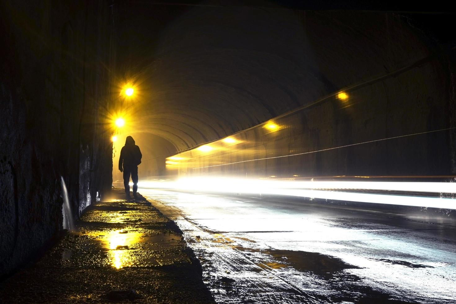 velho túnel úmido com a silhueta de um homem e trilhas de luz brilhante. foto