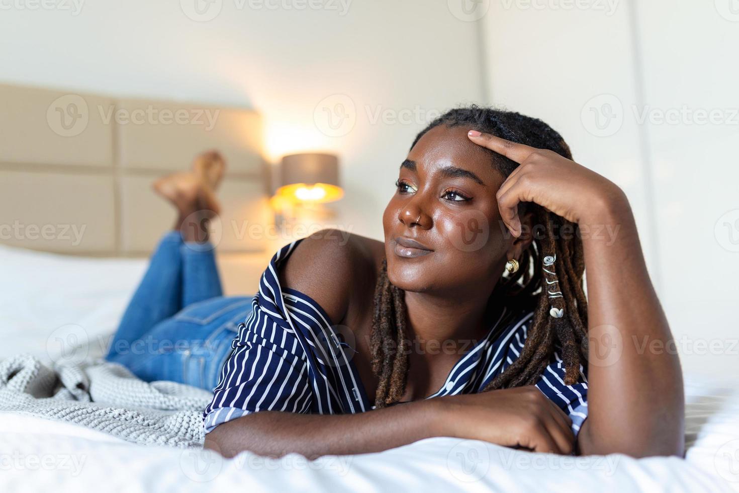 retrato do lindo e sensual africano jovem mulher deitado em cama. lindo mulher deitado dentro cama foto