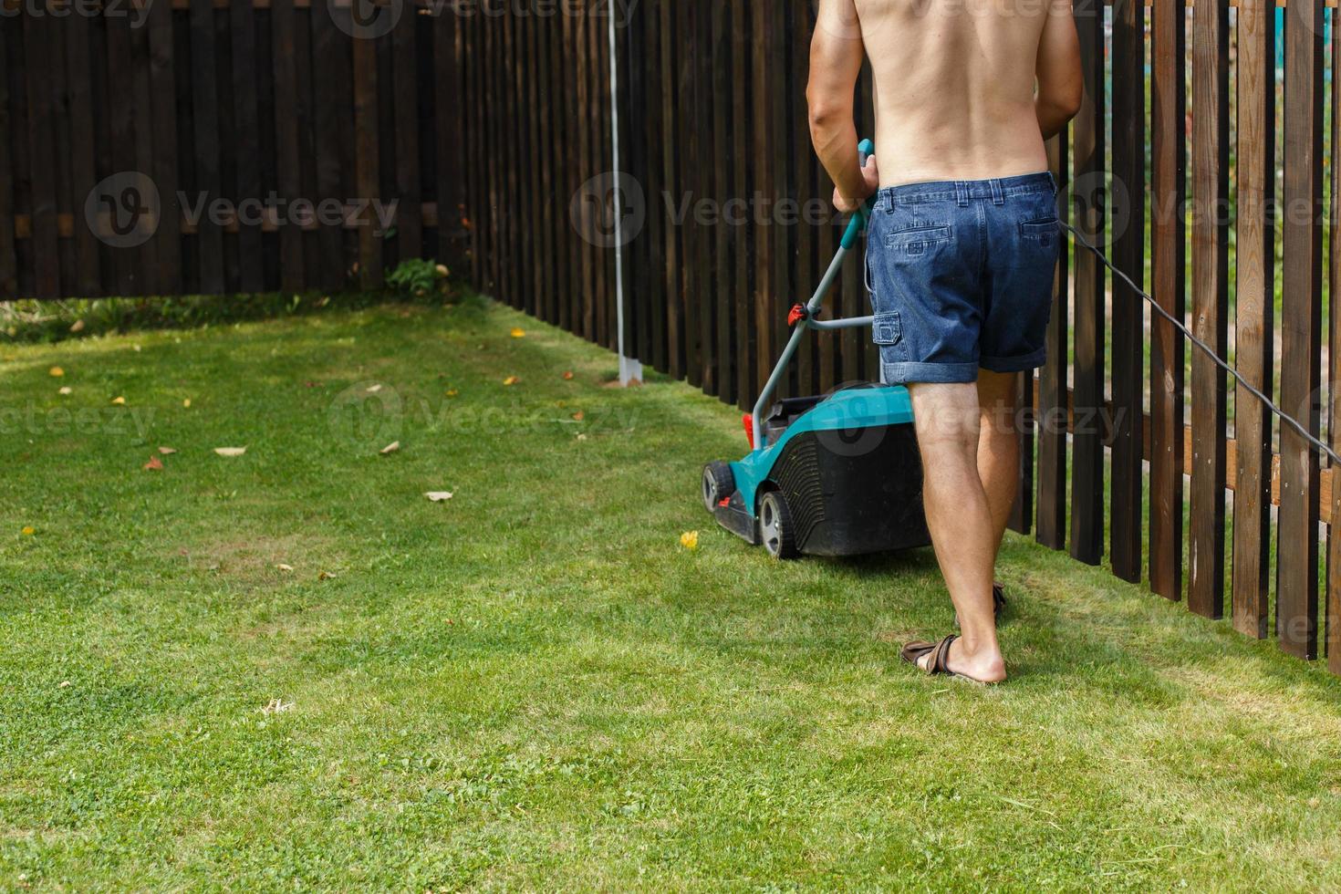 uma homem corta uma gramado com uma gramado cortador de grama foto