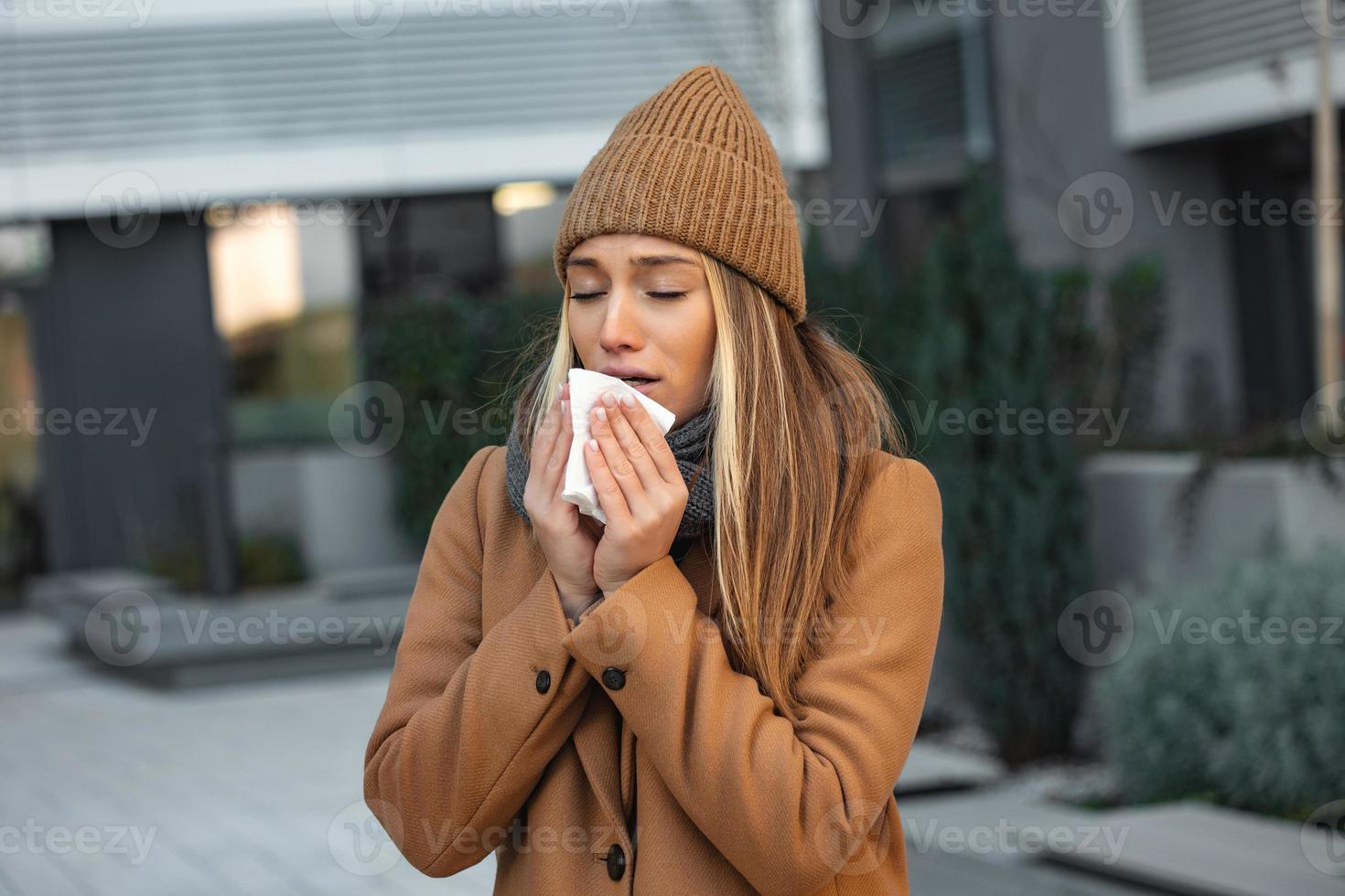 eu vou lindo jovem mulher espirros e sopro nariz dentro guardanapo. doente empresária dentro o negócio estilo espirrar às rua. pouco saudável funcionário. ar livre. vírus sintomas. frio doença. foto