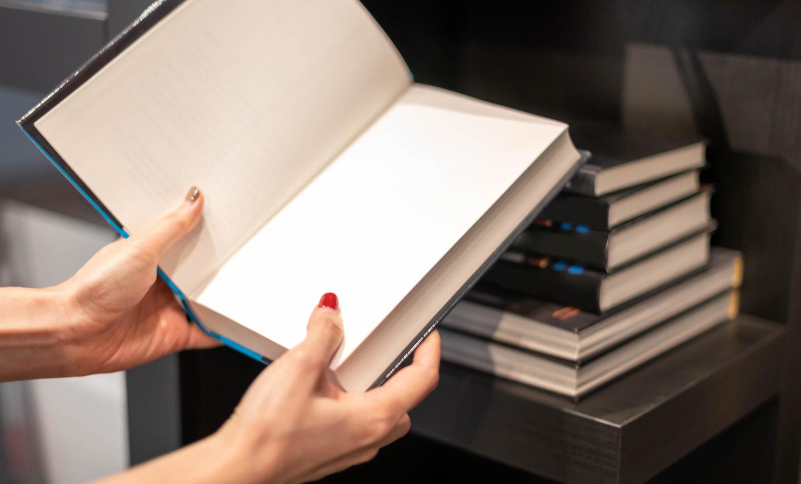 fêmea mão segurando caderno e lendo livro com a espaço área para relaxante e a conhecimento enquanto sentado em a sofá dentro público biblioteca. foto