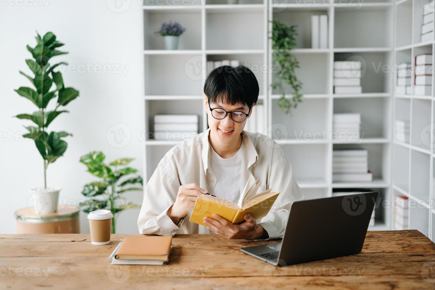 bonito e talentoso jovem ásia homem aluna trabalhando em dele projeto atribuição, usando computador portátil e tábua para procurar a conectados informações. foto